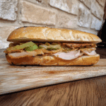Panino con porchetta su tagliere di legno, visto da vicino